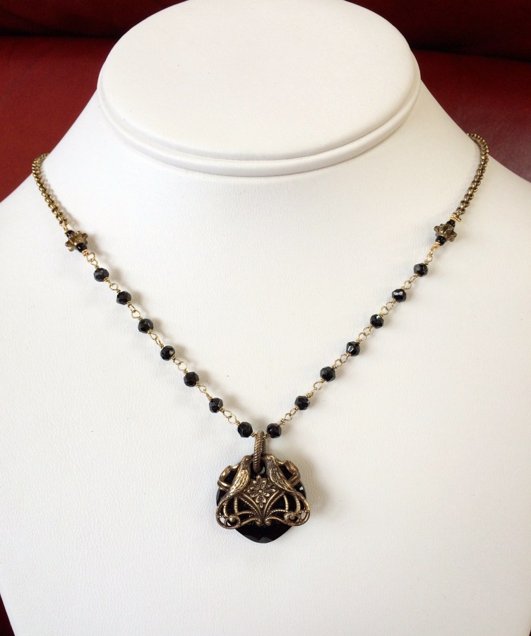 Lovebirds Necklace Two antiqued brass birds perch atop a jet black Swavorski Crystal which dangles from wire wrapped shining spinal faceted rondelles.