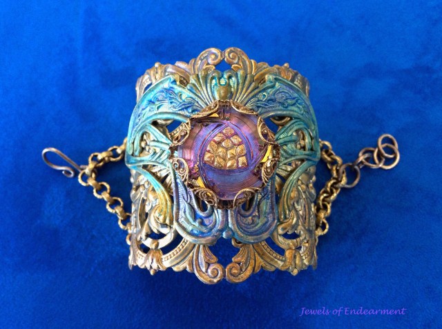 Winged Filigree Nouveau Fan Bracelet This romantic cuff has a vintage look to it with layers of stamped brass painted with shades of amethyst and aqua. Rivets are used to fasten the layers together.